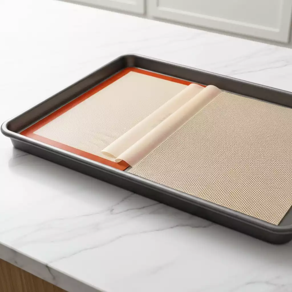 Assortment of cookie sheet liners including silicone mat, parchment paper, and perforated mat on a baking sheet, clean image